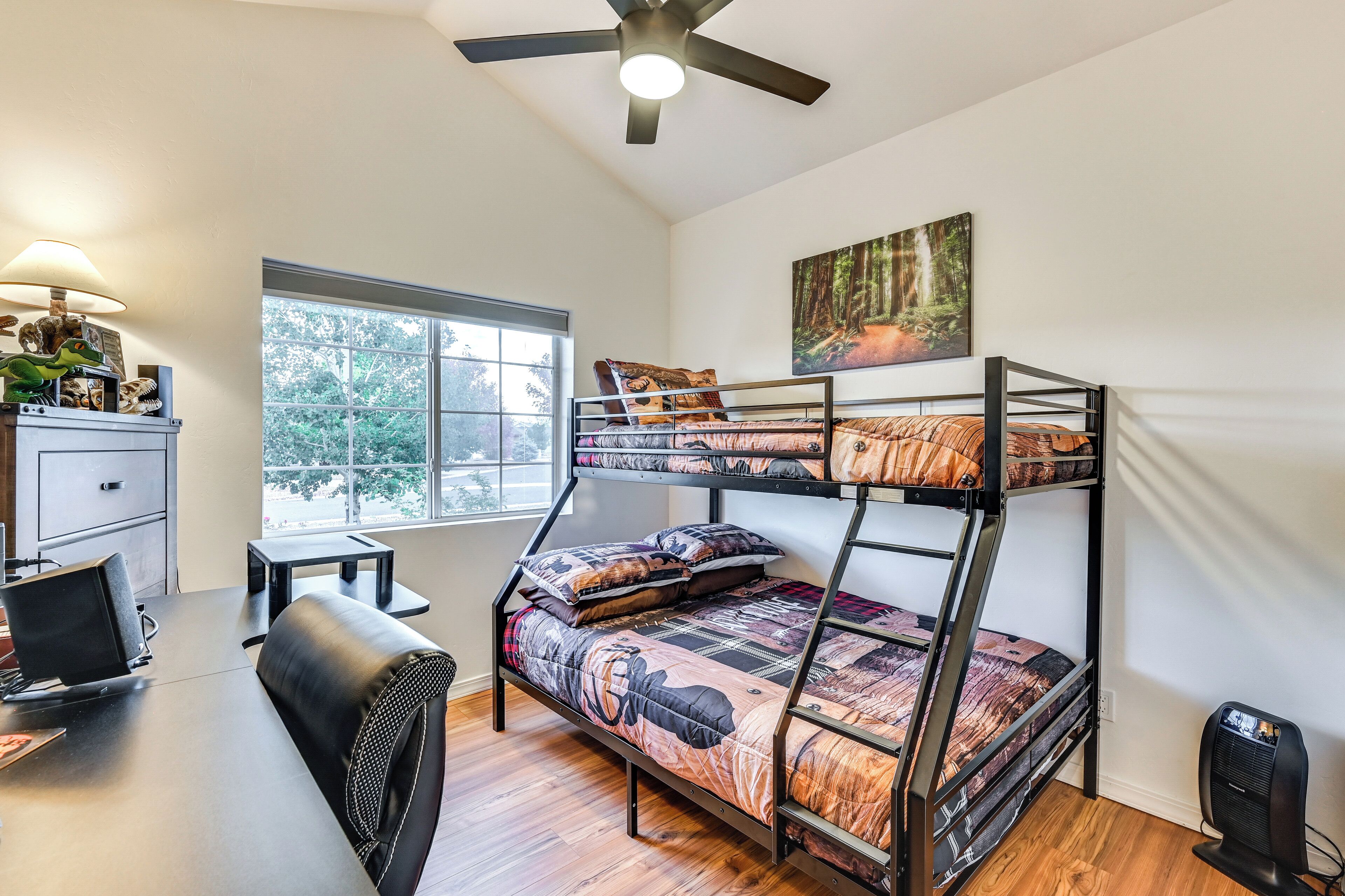 A bunk bed room with a desk, chair, and a fan.