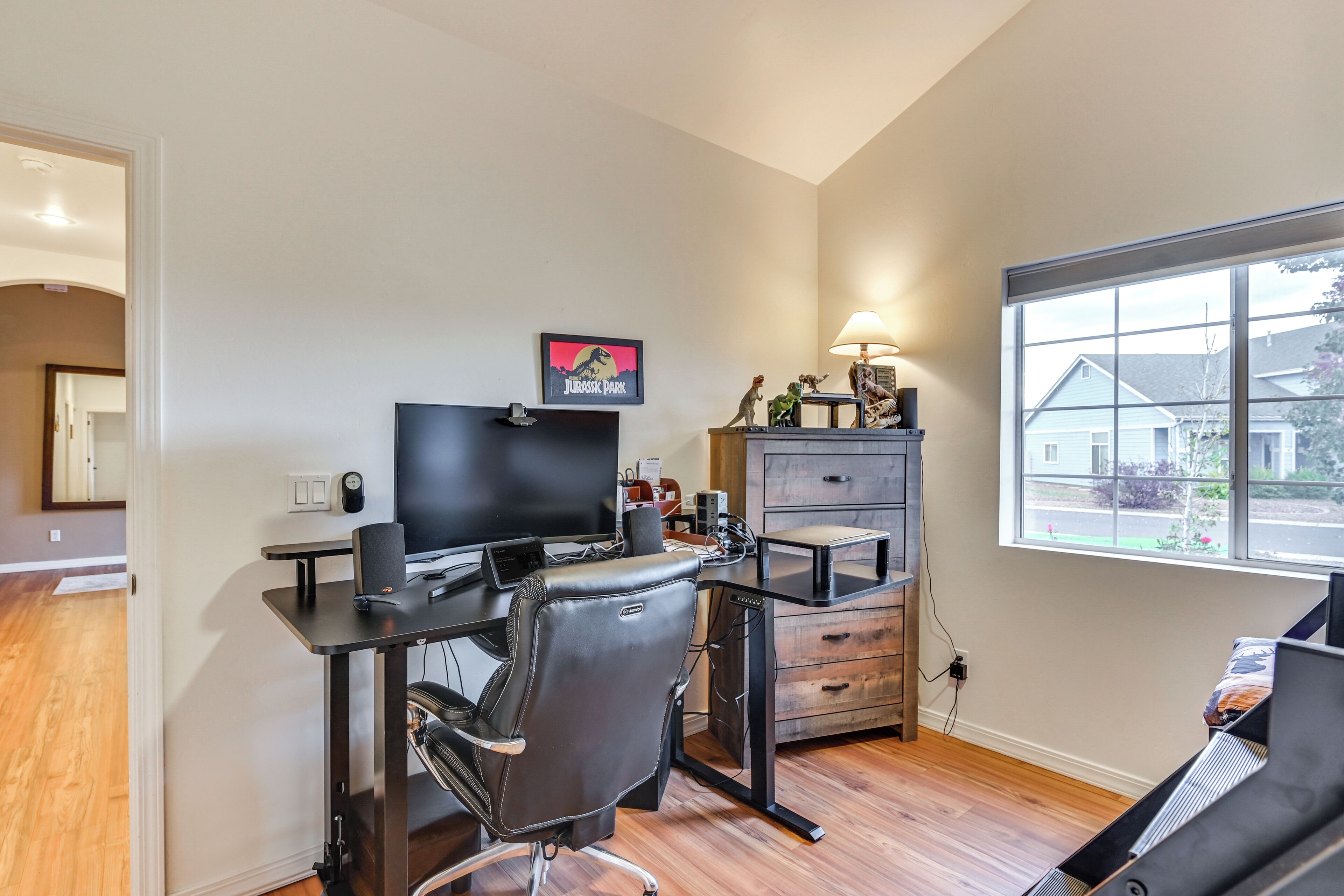 A home office with a desk, chair, computer, and a window with a view of houses.