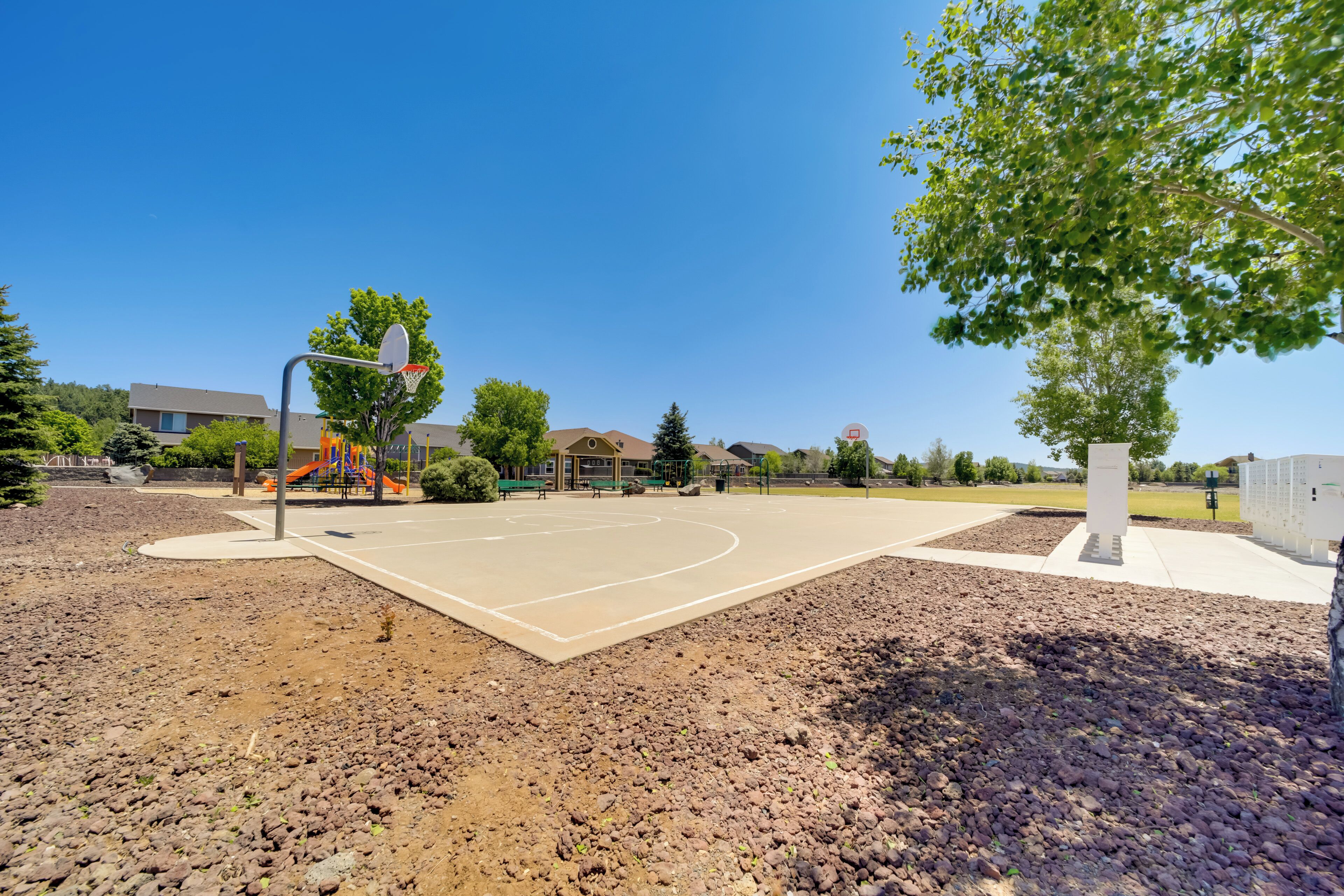 Ein Basketballplatz im Freien mit blauem Himmel, umgeben von Bäumen und Gebäuden.