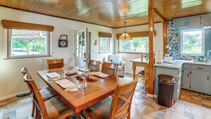 A dining area with a wooden table set for four, surrounded by chairs, and a kitchen area with a sink and cabinets. - Group Retreat on Wolf Lake! Paddle, Fish & BBQ (Jackson)