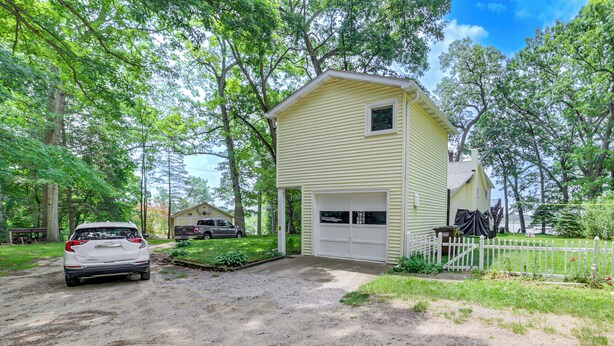 A single-story yellow house with a garage, surrounded by trees and a gravel driveway. - Group Retreat on Wolf Lake! Paddle, Fish & BBQ (Jackson)