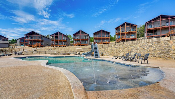 A pool area with a water slide, lounge chairs, and a stone wall. - Branson Gem w/ Hot Tub Access & Private Boat Slip! (Branson)