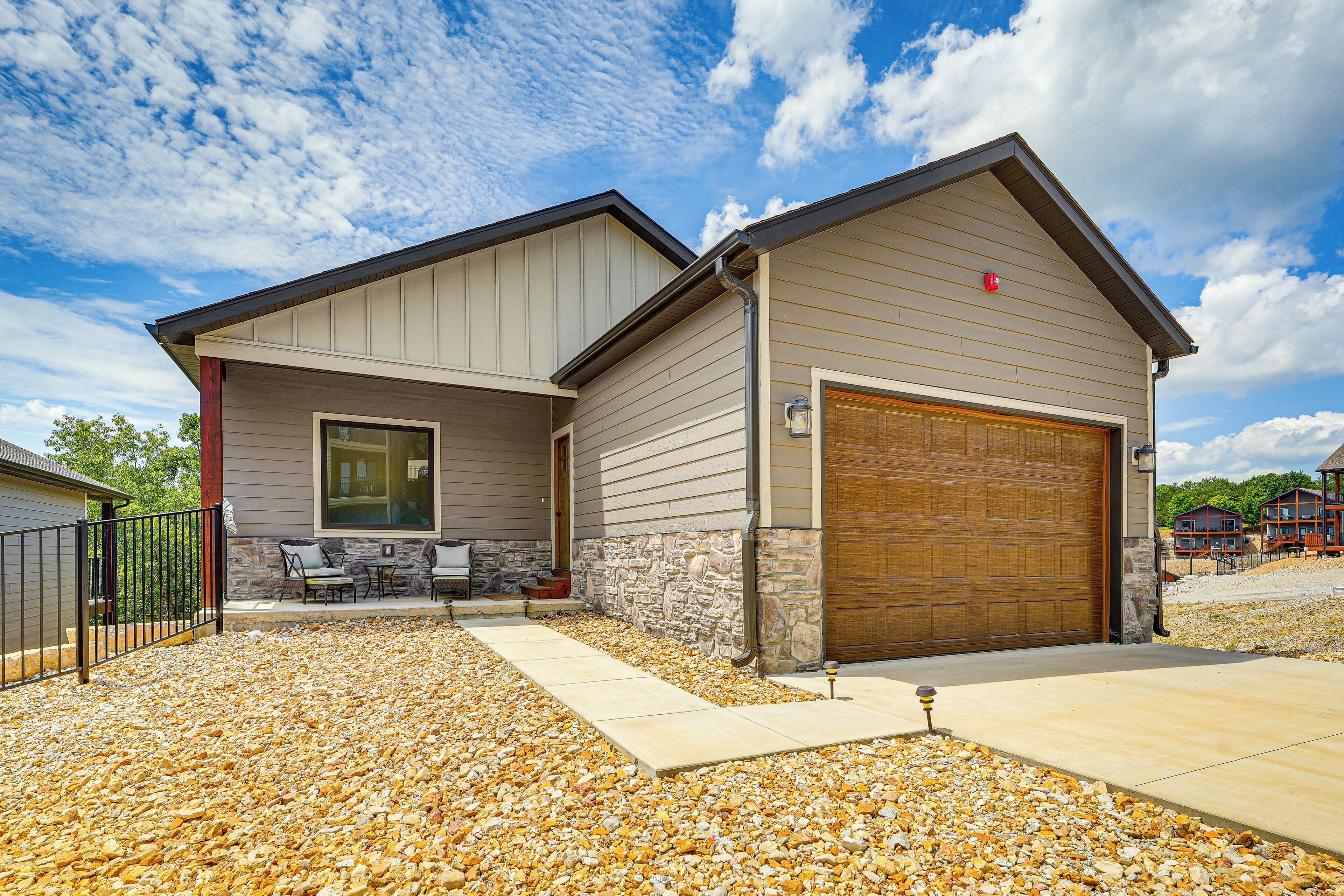 A two-story house with a garage, stone foundation, and a patio with outdoor furniture.