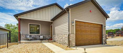 A two-story house with a garage, stone foundation, and a patio with outdoor furniture.