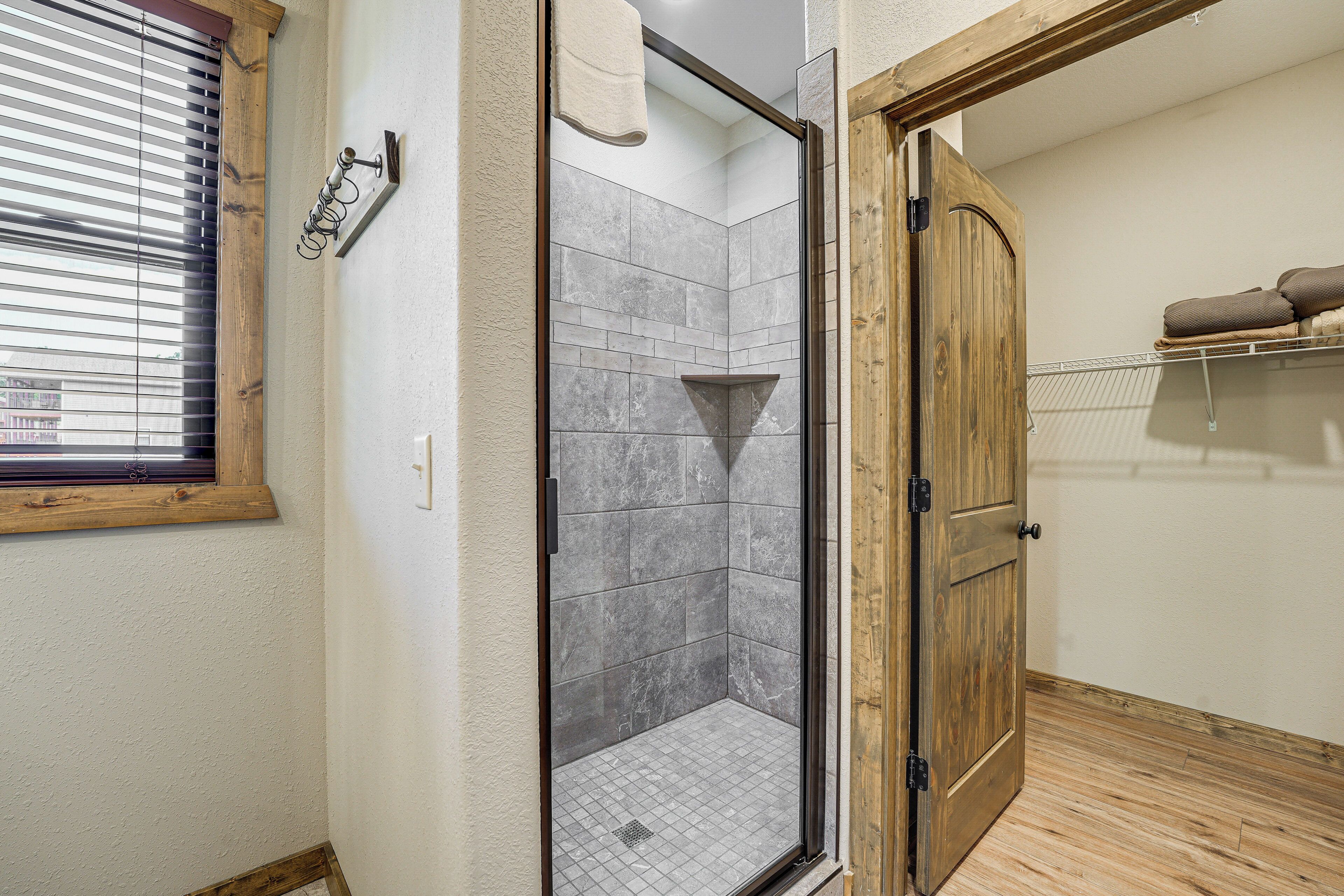 A shower with a glass door, a wooden door, and a towel rack on the wall.