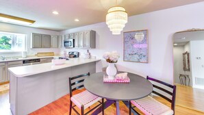 Una cocina moderna con armarios blancos, una isla central y un comedor con una mesa redonda y sillas.