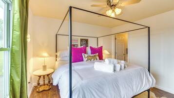 A four-poster bed with white bedding and a tiger print pillow, a ceiling fan, and a nightstand with a lamp.