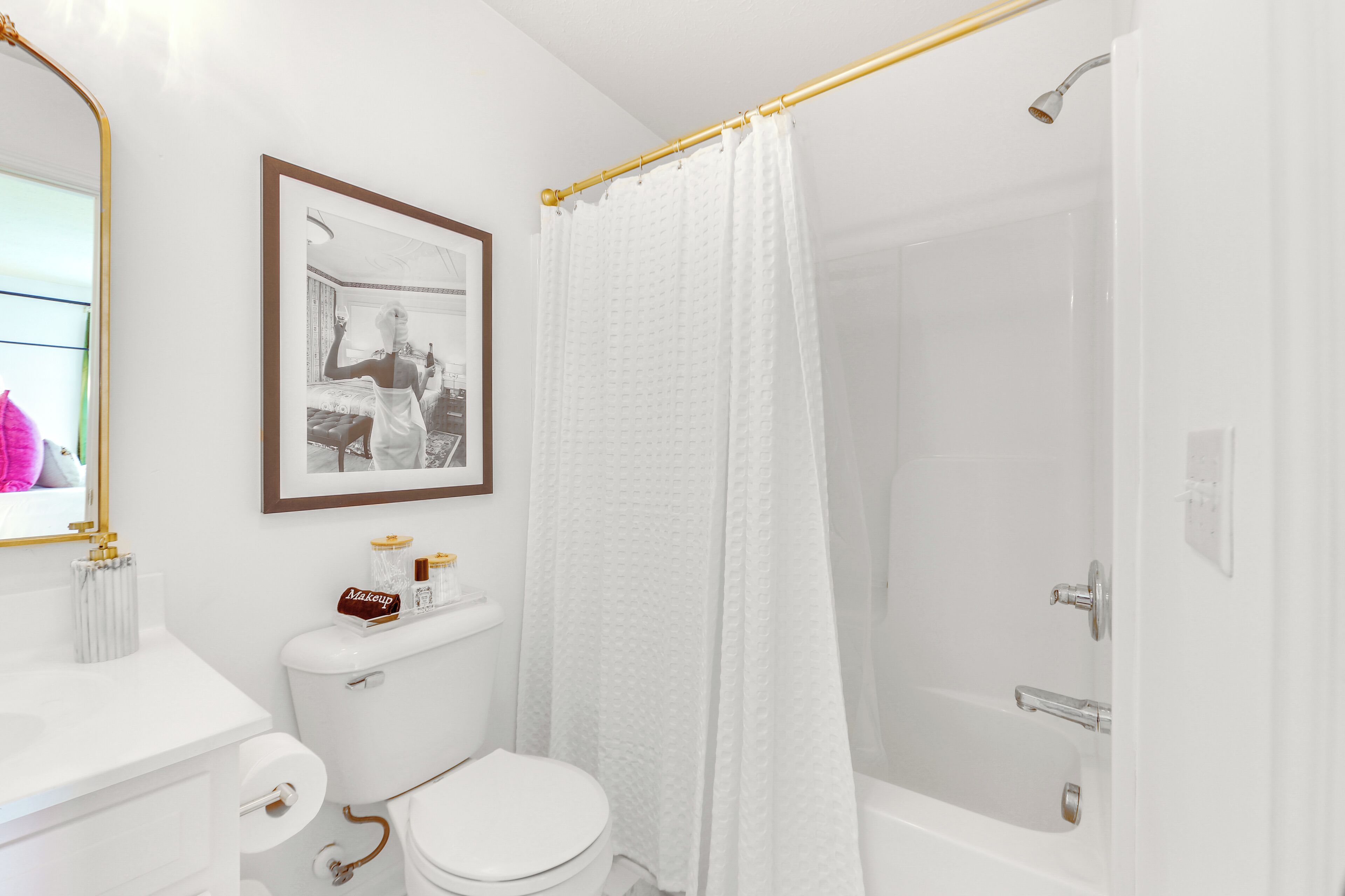 A bathroom with a toilet, a framed picture on the wall, a shower curtain, and a bathtub.