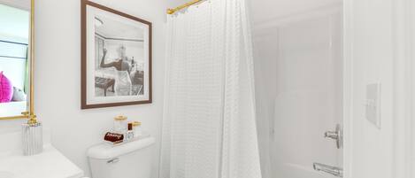 A bathroom with a toilet, a framed picture on the wall, a shower curtain, and a bathtub.