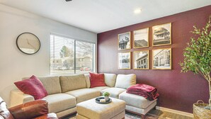 Un salon comprenant un canapé d’angle, un pouf, un fauteuil en cuir et une grande fenêtre avec des stores.