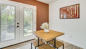 Un coin repas avec une table et des bancs en bois, un vase blanc contenant une plante et une œuvre d’art encadrée accrochée au mur.