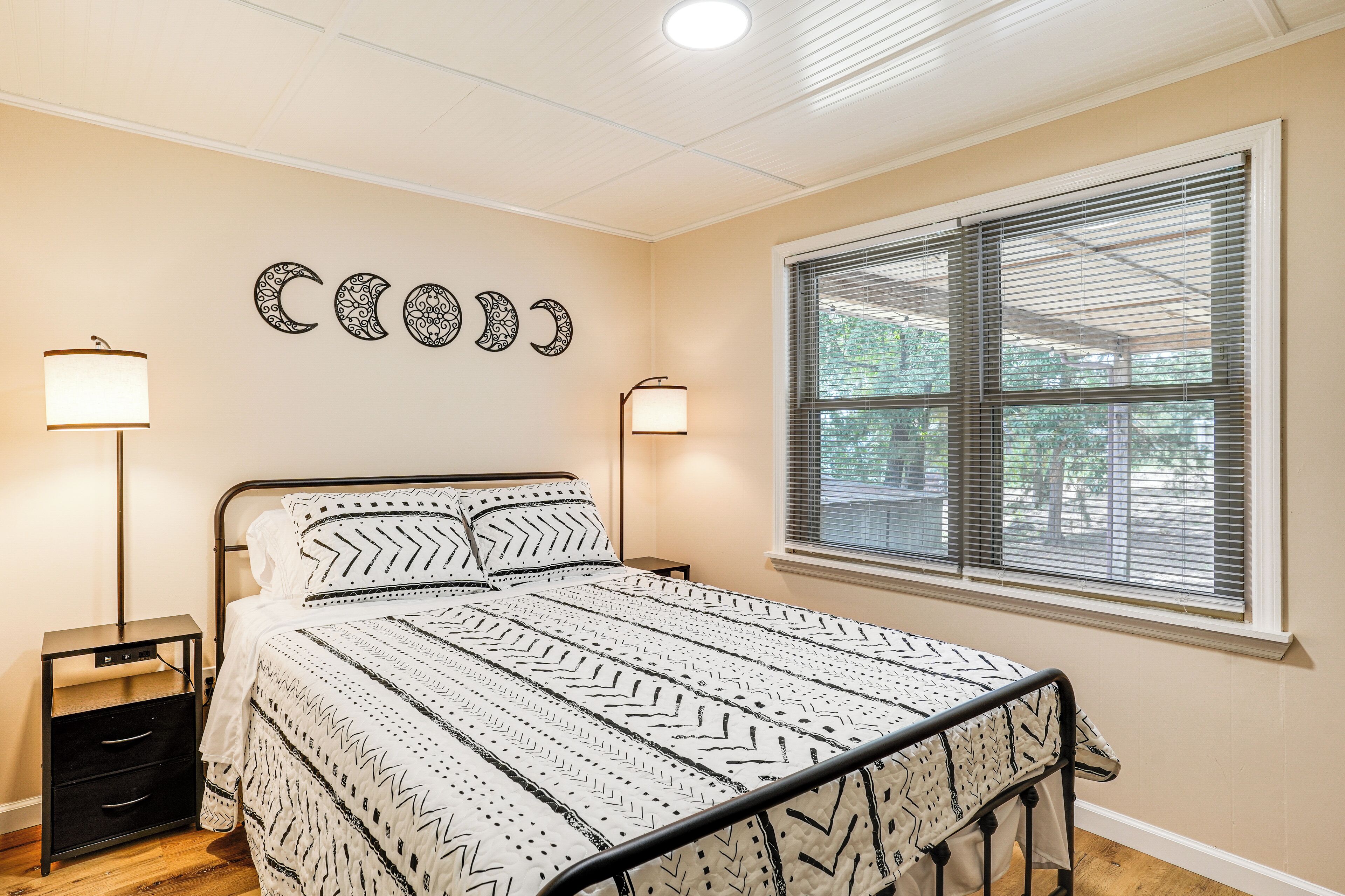 A bedroom with a bed, bedside tables, wall art, and a window with blinds.
