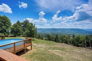 Terraza de madera con piscina, rodeada de árboles y vistas a montañas distantes.