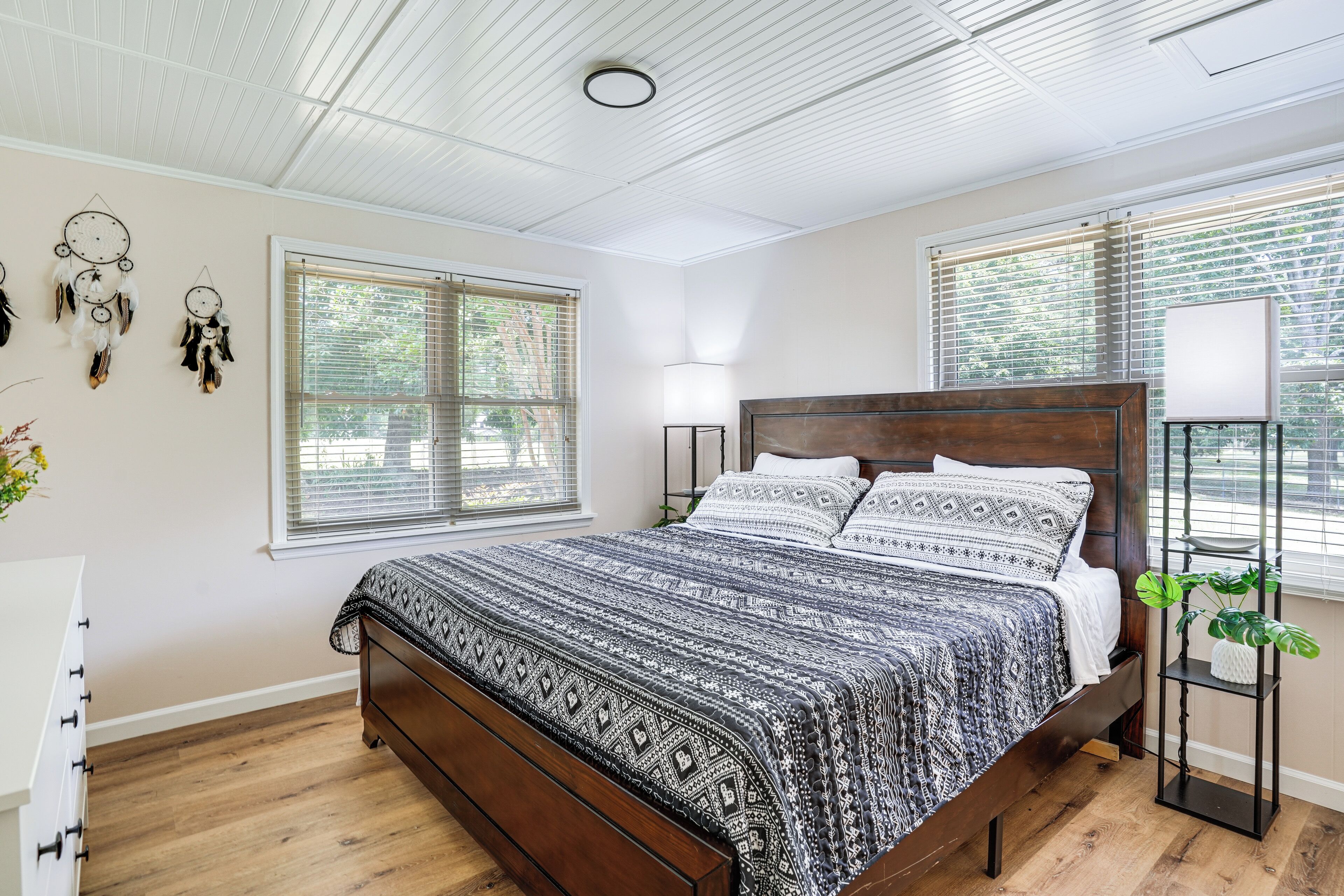 A bedroom with a wooden bed, patterned bedding, a bedside lamp, and a plant.