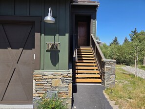 A house with a wooden staircase leading to a front door, a mailbox with the number 1601, and a stone wall.