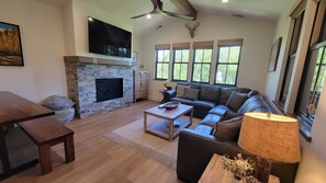 A spacious living room with a stone fireplace, a large flat-screen TV, a leather sofa, and a dining table.