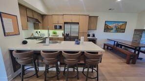 A modern kitchen with a central island, bar stools, a refrigerator, and a dining table.