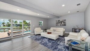 Ein geräumiges Wohnzimmer mit großem Fenster zum Pool, weißen Ledersofas und einem Glastisch.