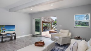 Ein modernes Wohnzimmer mit Flachbildfernseher, weißen Sofas und einer großen Schiebetür zu einer Außenpatio.