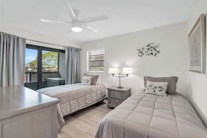 A bedroom with two beds, a desk, a ceiling fan, a window with blinds, and a nightstand with lamps. - E-234 -Deluxe Updated Condo With Beautiful Views! (Naples)