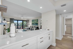 Une cuisine moderne avec des meubles blancs, un îlot central et une vue sur l’extérieur.