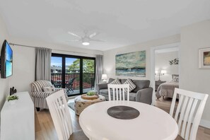A modern living room with a round dining table, striped armchairs, a grey sofa, and a ceiling fan. - E-234 -Deluxe Updated Condo With Beautiful Views! (Naples)