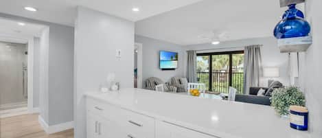 A modern kitchen with white cabinetry, a central island, and a large window with a view of the outdoors.