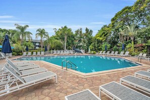 A rectangular swimming pool surrounded by lounge chairs and umbrellas, with a tiled deck and tropical vegetation. - F-237 - Deluxe Condo - Amazing Views and Sleeps 6 (Naples)