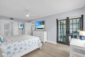 Quarto com cama, penteadeira, televisão e porta de vidro corrediça para uma varanda.