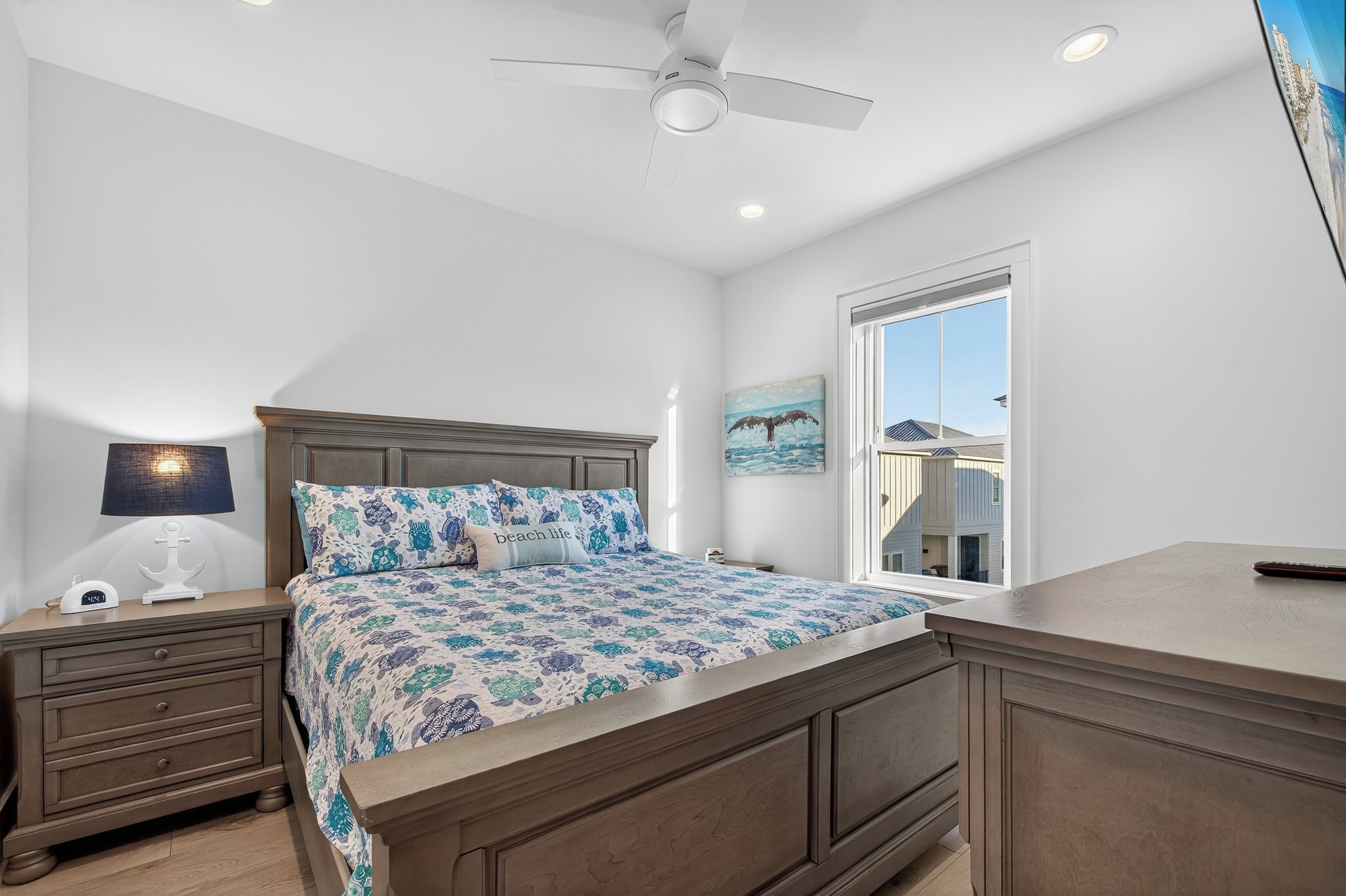A bedroom with a bed, nightstands, a ceiling fan, and a window with a view of a building.