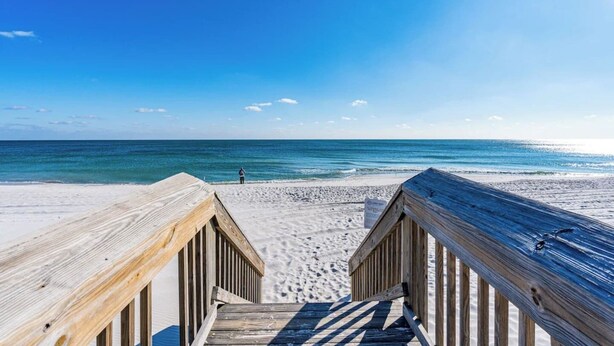 A wooden boardwalk leading to a beach with a clear view of the ocean and a person standing at the water's edge. - Beach Across St | Pool + Hot Tub | Sleeps 12 (Gulf Shores)