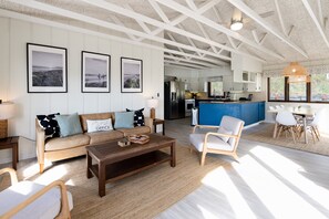 A modern living room with a sofa, coffee table, and chairs, a kitchen in the background, and framed pictures on the wall.