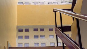 Una escalera con barandilla de metal que sube a un rellano con pared blanca y ventana de diseño celosía.