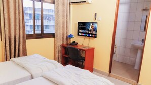 Habitación de hotel con dos camas, un escritorio con silla, televisor montado en la pared y un baño a la vista a través de una puerta abierta.