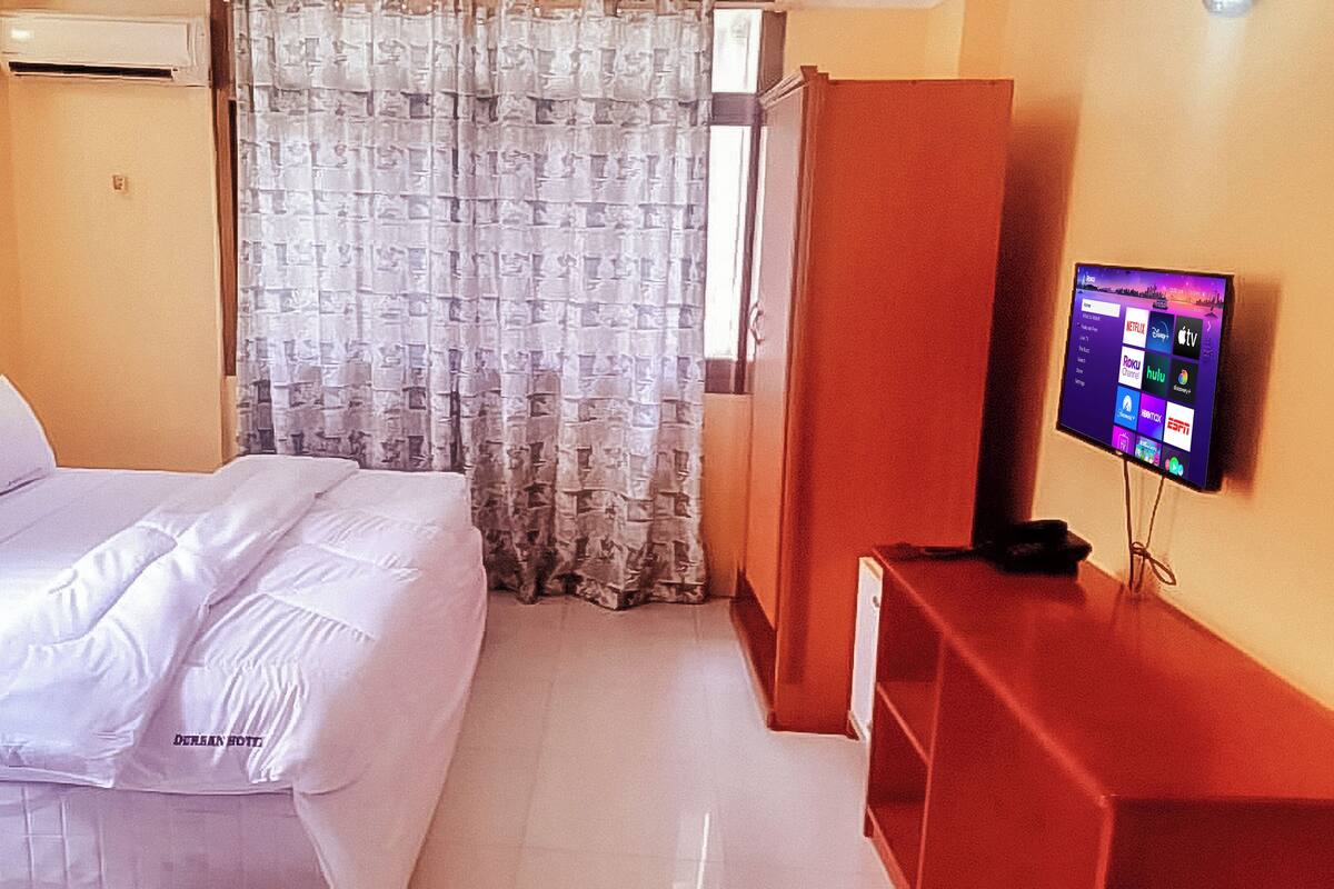 Een hotelkamer met een bed, een televisie op een standaard, een kledingkast en een gordijn.