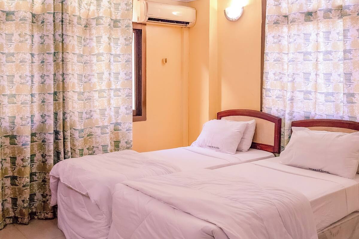 Een tweepersoonsbed met witte beddengoed, een houten hoofdbord en een airconditioner bevestigd aan de muur.