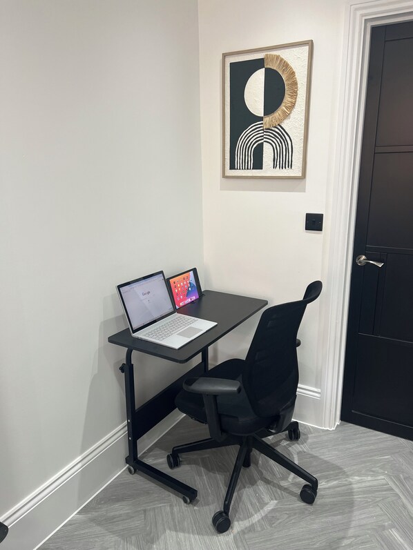 A workspace with a desk, two laptops, a black office chair, and a framed abstract artwork on the wall. - Stylish Flat in London, sleeps 4
(Hornchurch)