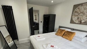 A modern hotel room with a neatly made bed, a black wardrobe, a standing mirror, and a large abstract painting on the wall. - Stylish Flat in London, sleeps 4
 (Hornchurch)