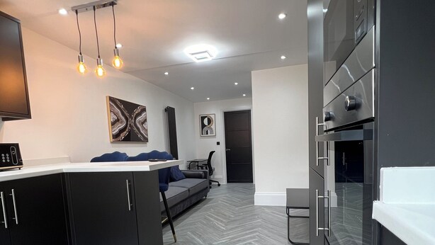 A modern kitchen with dark cabinetry, a central island, and a built-in oven. - Stylish Flat in London, sleeps 4
 (Hornchurch)