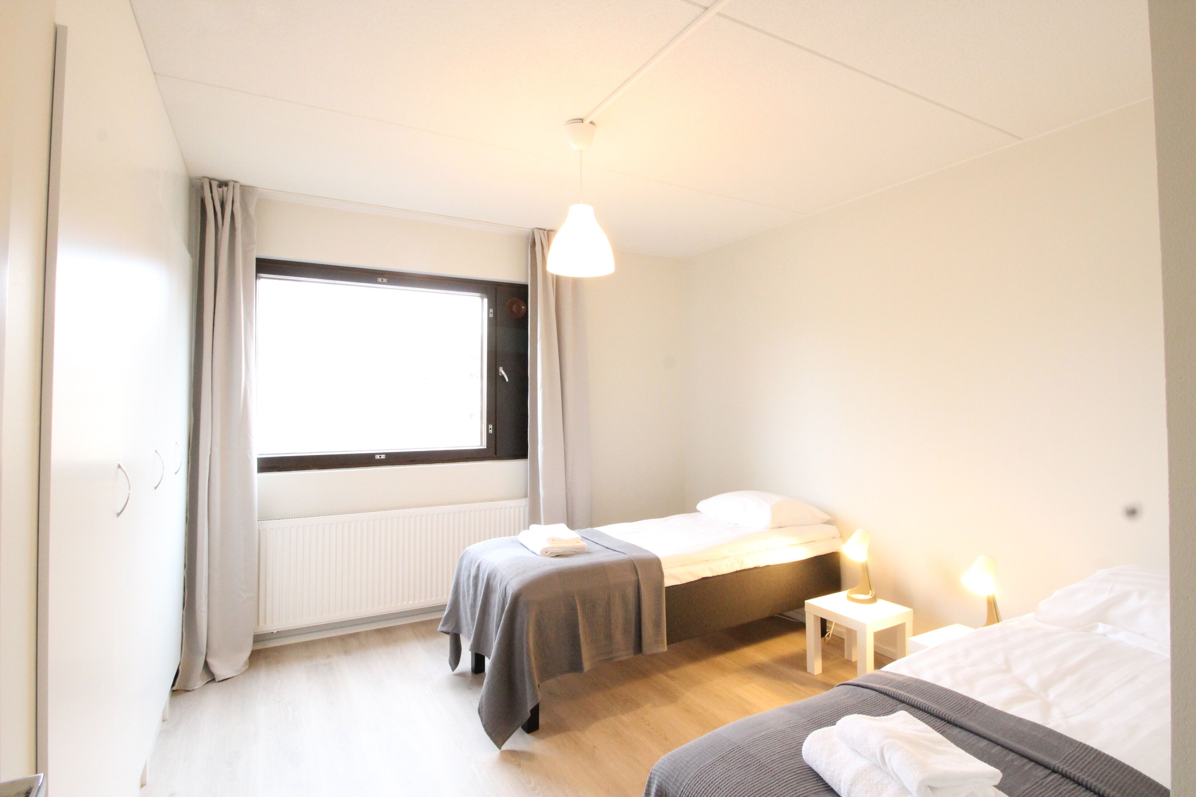 Un dormitorio con dos camas, una ventana, un radiador y lámparas de noche.