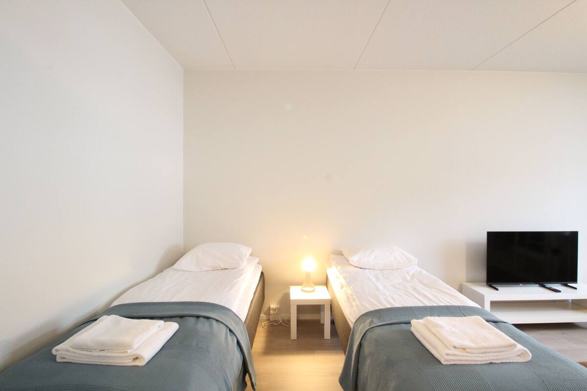 A twin room with two single beds, a bedside table with a lamp, and a TV on a stand.