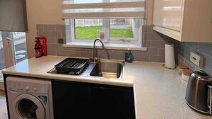 Een compacte keuken met een ingebouwde wasmachine, een spoelbak en een raam met zonwering.