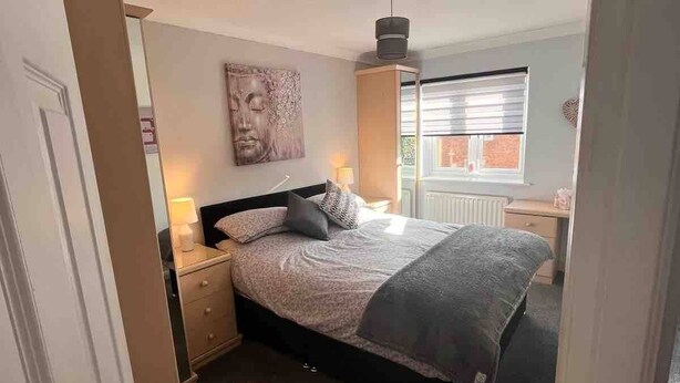 Een slaapkamer met een bed, nachtkastjes, een dressoir, een raam met jaloezieën en een plafondlamp.