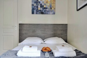 A neatly made bed with white pillows, a gray blanket, and a tray of croissants. - Résidence Paris MAGENTA (Paris)