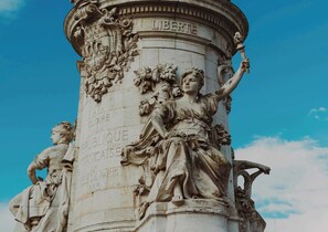 A detailed stone monument with inscriptions and sculptures, including a figure holding a torch and another with a laurel wreath. - Résidence Paris MAGENTA (Paris)