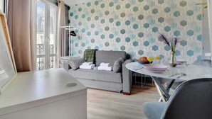 Un salon moderne avec un canapé gris, une table à manger en verre et un mur orné d’un motif.