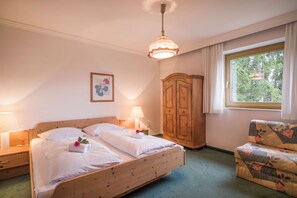 A hotel room with a wooden bed, a nightstand, a wardrobe, a chair, and a window with curtains.