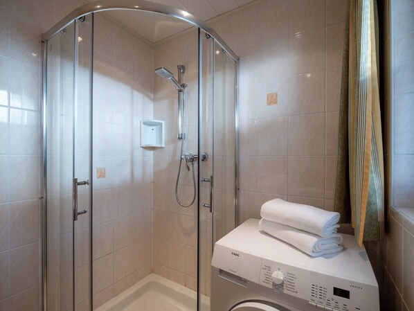 Un baño moderno con ducha de vidrio, lavadora integrada y toallas ordenadas sobre un mostrador.