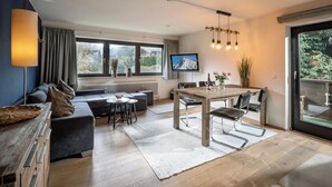 Un salon moderne comprenant un canapé, une table à manger et des chaises, un téléviseur et une grande fenêtre offrant une belle vue.
