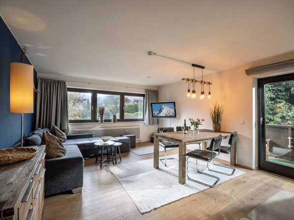 Een moderne woonkamer met een bank, eettafel, stoelen, een televisie en een groot raam met uitzicht.